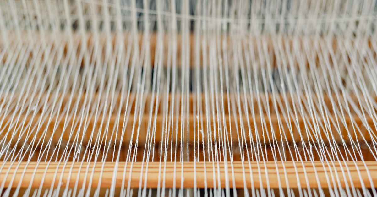 Métier à tisser traditionnel avec des fils de soie et de laine tendus, dans un atelier lumineux.
